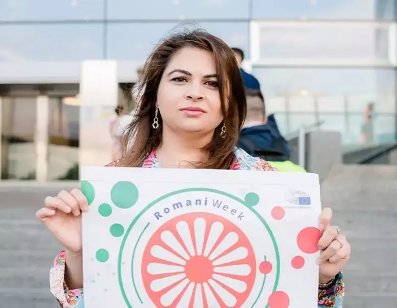 Woman holding Romani Week sign outdoors.